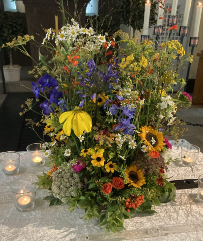 Diese spätsommerliche Urne ist etwas luftiger gesteckt. Ihre Blumen sind Sonnenblumen, Rudbeckien, Mutterkraut, Dill, Rittersporn, Eisenhut, Bartnelken, Flammenblumen, Rose, Sonnenhut, Goldrute, Rainfarn, Sterndolden, Montbretien, Vogelbeeren und Schmucklilien.